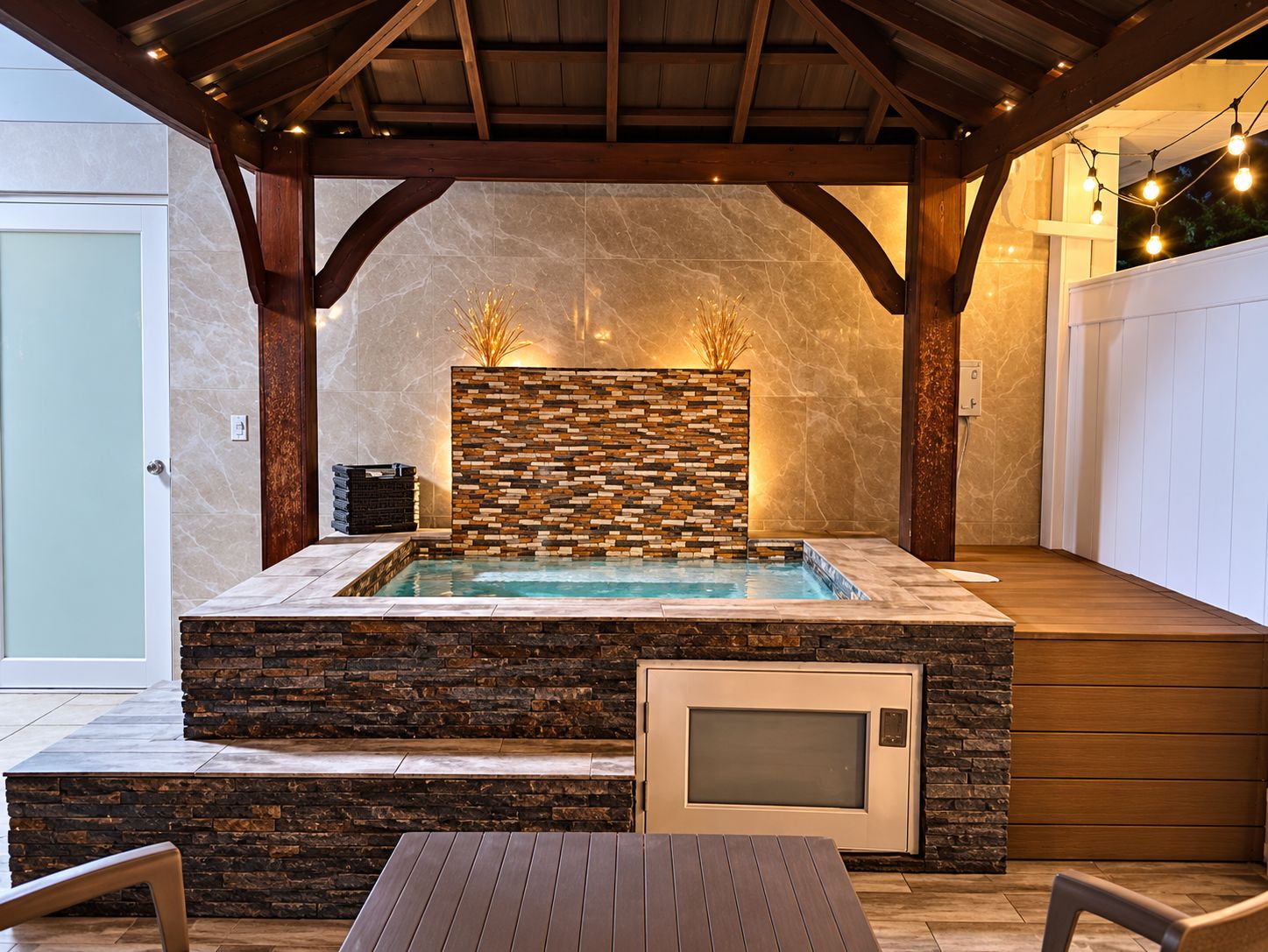 Un jacuzzi con un muro de piedra de fondo, una terraza de madera y un área de estar cubierta.