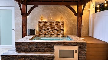 Un jacuzzi con un muro de piedra de fondo, una terraza de madera y un área de estar cubierta.