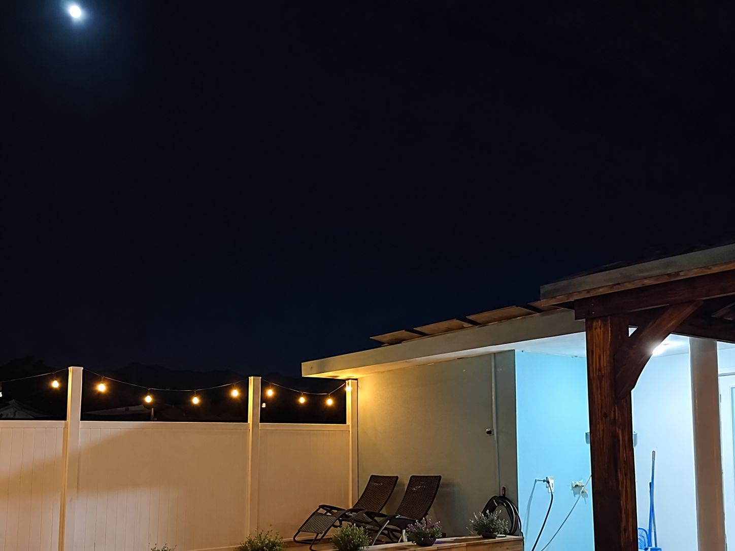 An outdoor patio area with string lights, two lounge chairs, and a pergola structure.