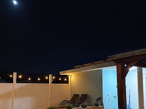 An outdoor patio area with string lights, two lounge chairs, and a pergola structure.