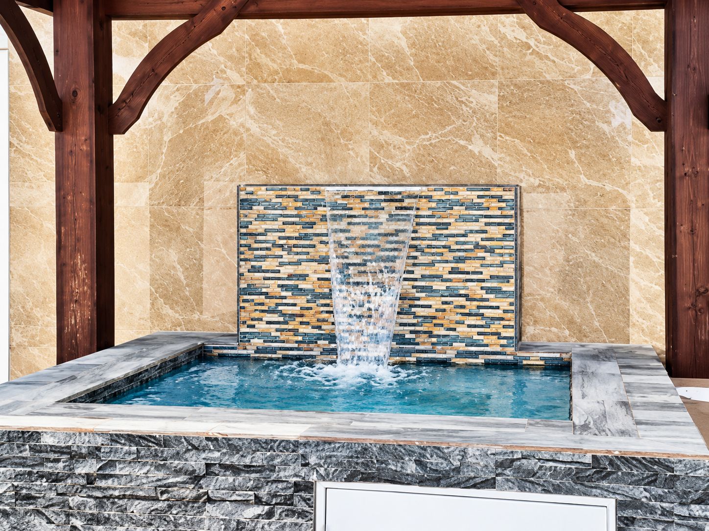 Private hot tub with waterfall under a wooden gazebo.