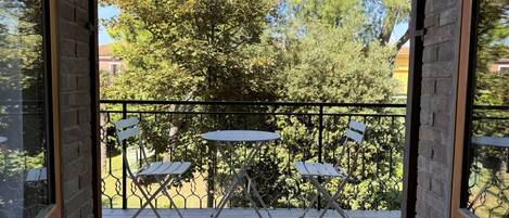 An open balcony with a table and chairs, a metal railing, and a view of trees and buildings.