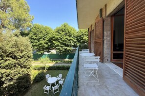 A balcony with white metal chairs and tables, a swimming pool, and a view of trees and a building. - SE280 – Senigallia, comfortable one-bedroom apartment with wi-fi (Senigallia)