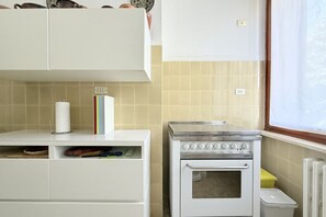 Une cuisine avec des meubles blancs, une cuisinière et une fenêtre.