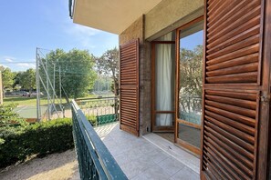 Ein Balkon mit Blick auf ein Sportfeld, eine Tür mit Holzläden und ein Fliesenboden.