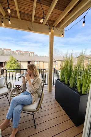 A wooden deck with a wicker chair, a black planter with plants, and a clear view of buildings in the background. - Our Nest-Pointe Royale Resort-Pools/Hot Tub/Golf (Branson)