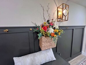 A dark-colored bench with a woven basket of flowers and a wall-mounted light fixture. - Fire Fly Loft by Branson Landing-Waterfront (Branson)