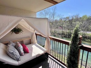 A balcony with a cushioned seating area, a white canopy, and a view of a river and trees. - Fire Fly Loft by Branson Landing-Waterfront (Branson)