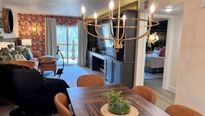 Un coin repas avec une table en bois, des chaises et un lustre. On aperçoit un canapé et un fauteuil de massage à l’arrière-plan.