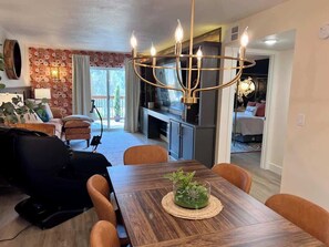 A dining area with a wooden table, chairs, and a chandelier. There is a sofa and a massage chair in the background. - Fire Fly Loft by Branson Landing-Waterfront (Branson)
