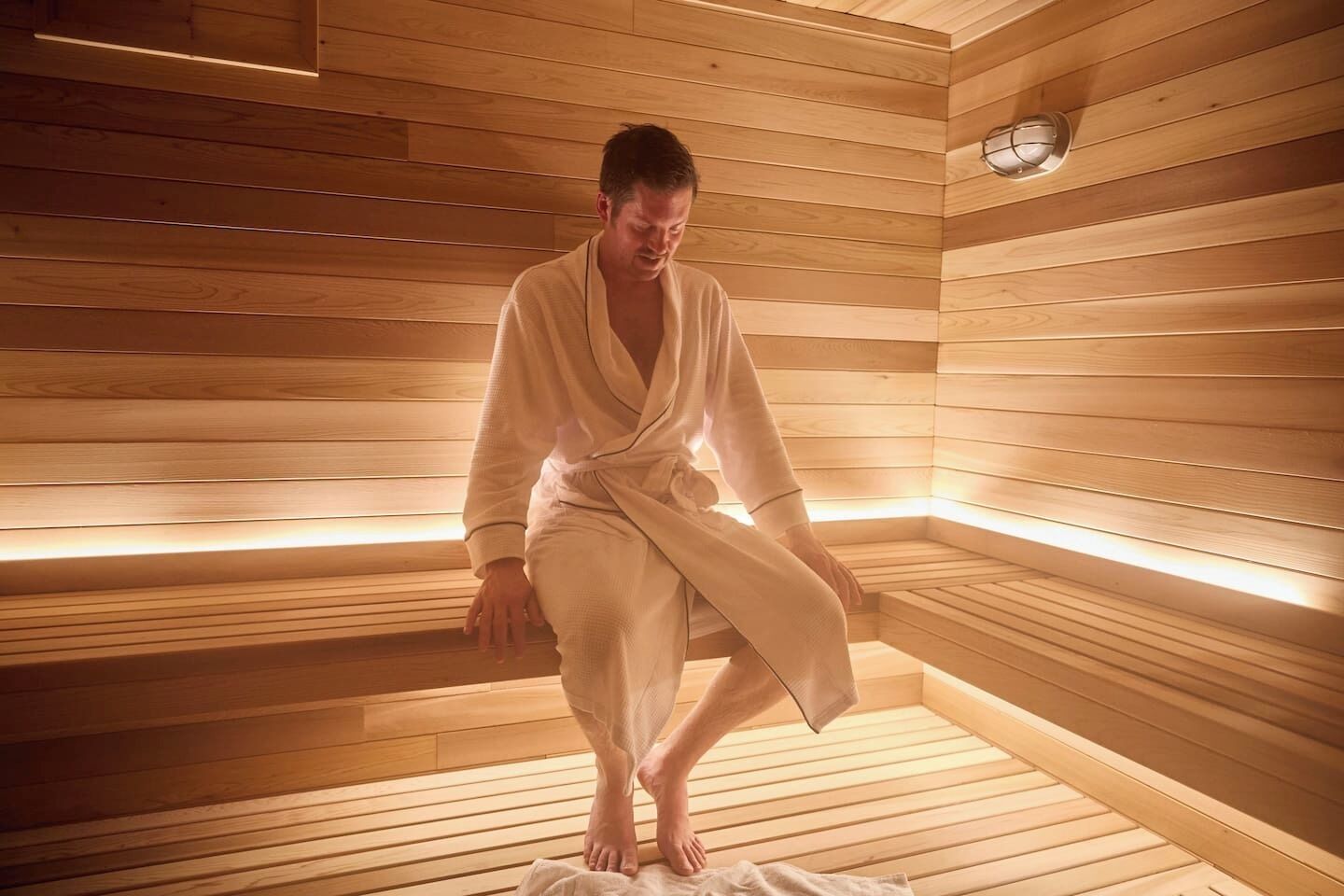 Une personne assise dans un sauna en bois, dont les murs sont constitués de lattes et qui est équipé d’un banc.
