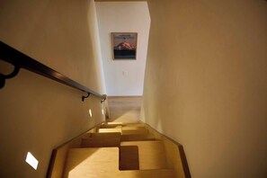 Un escalier en bois, doté d’une rampe, mène à un palier où est accrochée une image encadrée au mur.