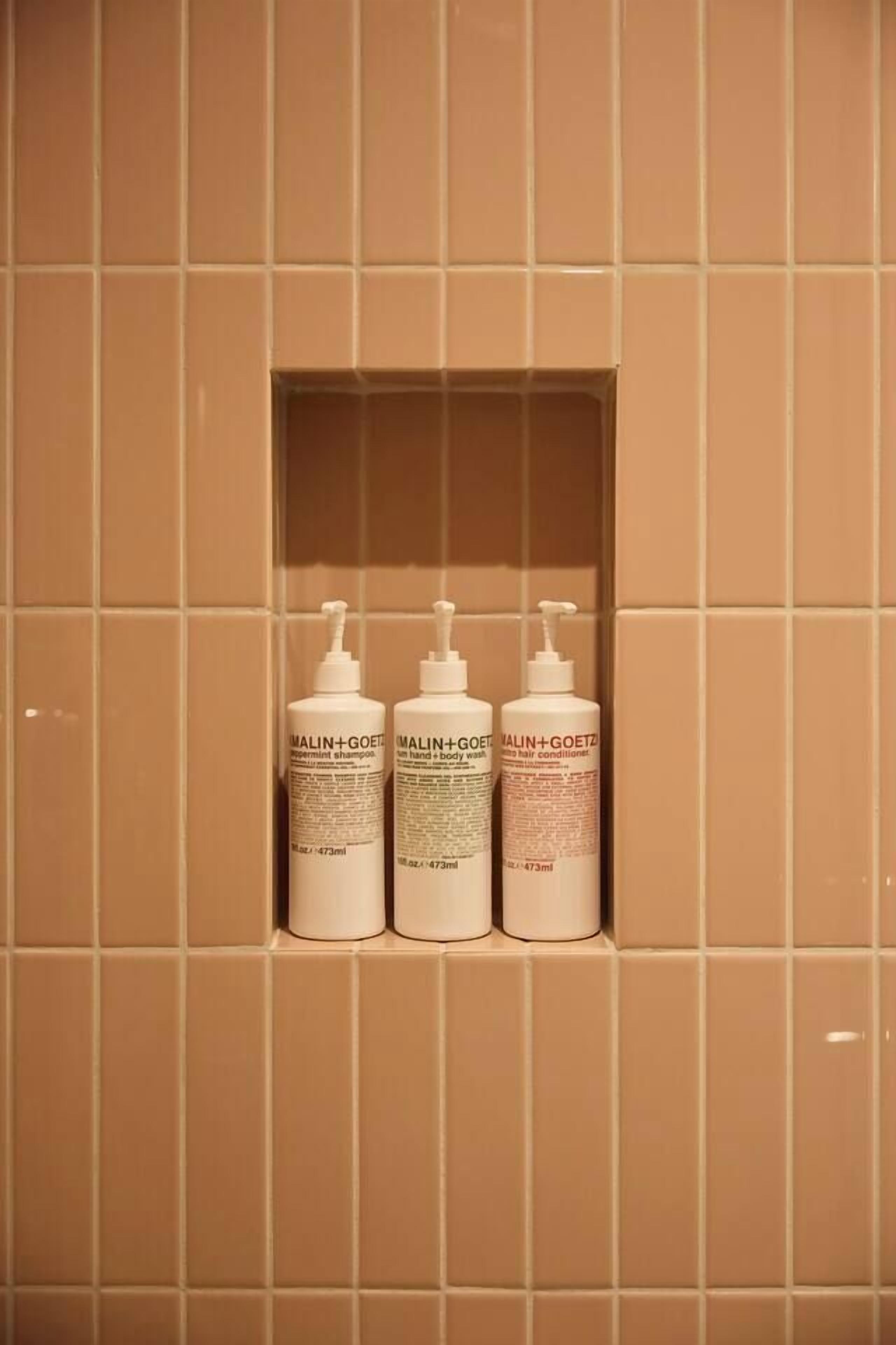 Three bottles of MALIN+GOETZ body wash in a tiled wall niche.