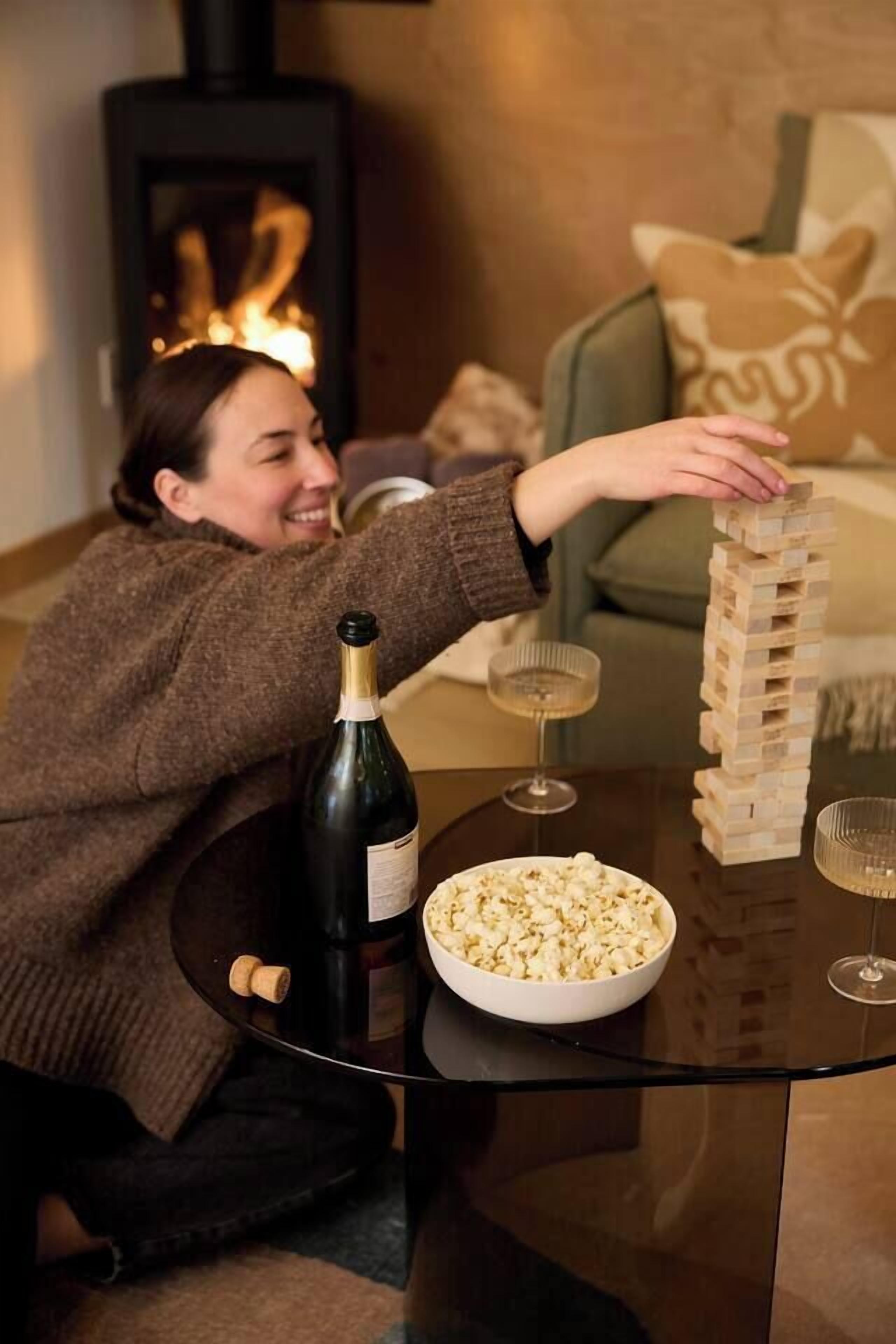 En person spiller Jenga på et bord med en flaske vin, en skål popcorn og glas.