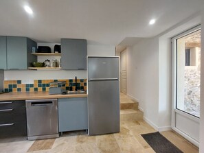 Cuina compacta amb rentaplats integrat, nevera i un frontissó de rajola.