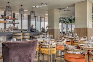 Un restaurant doté d’un bar, de plusieurs tables avec des chaises et offrant une vue sur l’extérieur grâce à de grandes fenêtres.
