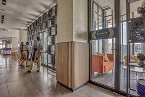 En hotellobby med modern design, med en stor entré av glas, en sittgrupp med en soffa och en dekorativ vägg med mönstrade paneler.