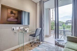 Une chambre moderne dotée d’un téléviseur à écran plat, d’un bureau en verre, d’une chaise, d’un canapé, d’une petite table et offrant une vue sur l’extérieur.