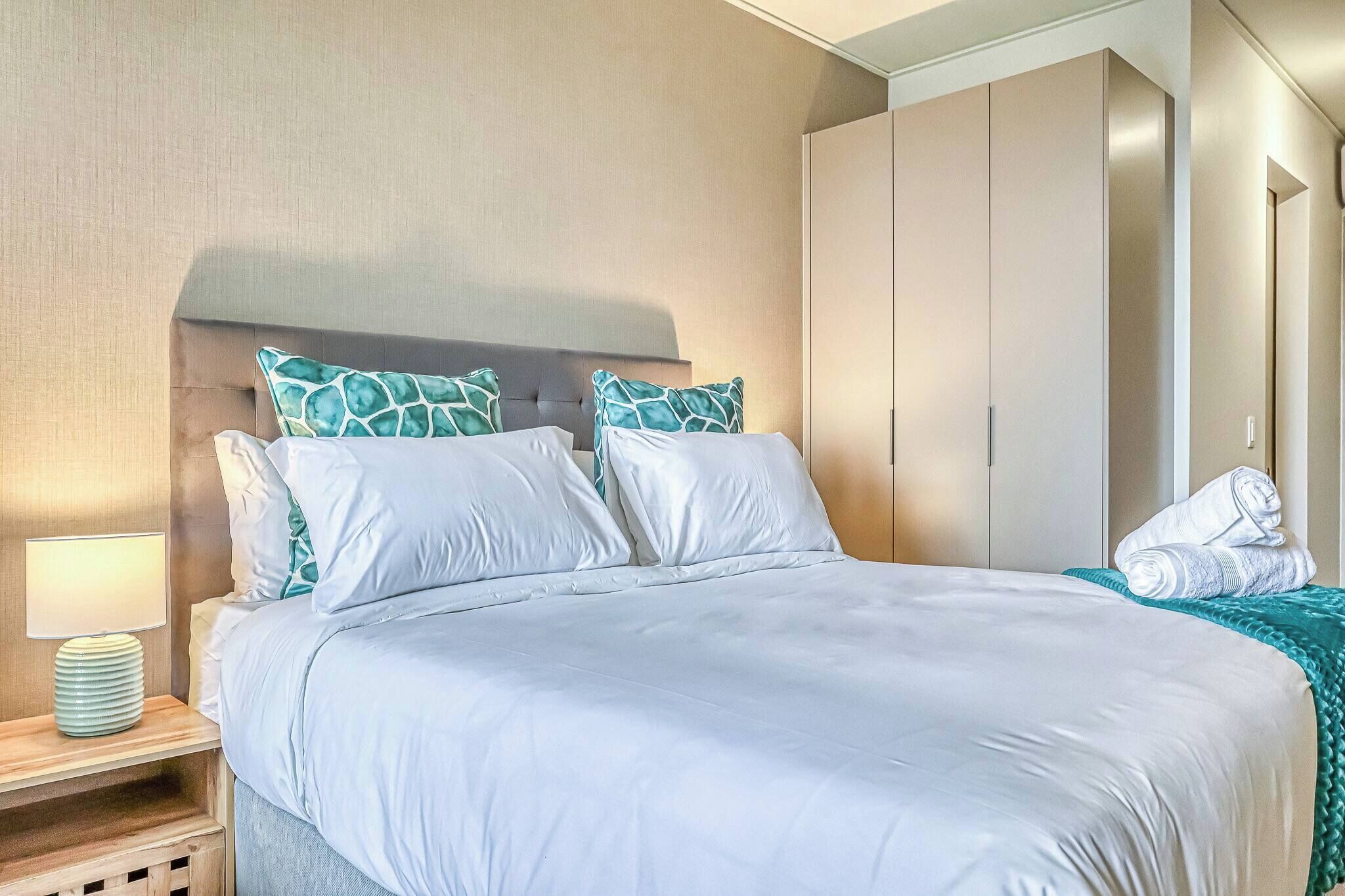 Una habitación de hotel con una cama, una mesita de noche, una lámpara, un armario y una toalla doblada sobre la cama.