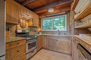 A kitchen with wooden cabinets, a stove, and a window overlooking greenery. - Aspen Peak Chalet | Lake Aspen, Foliage, Fire Pit (Innsbrook)