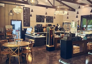 Kahvilan sisustus: puupöytiä, riippuvalaisimia, kahvitiskialue ja menutauluja.