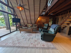 A spacious living room with a large window, a wooden ceiling, and a cozy fireplace.