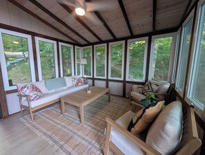 A room with a wooden ceiling, large windows, a sofa, a coffee table, and a chair.