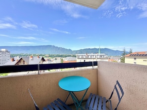 A balcony with a blue table and chairs, a view of a town and mountains in the background. - T2 Thermes et centre Aix-les-Bains parking (Aix-les-Bains)