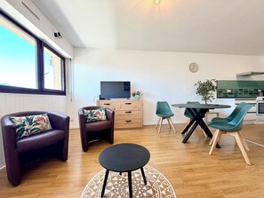 A modern living room with a TV, wooden cabinet, two leather chairs, a round table, and a kitchen in the background. - T2 Thermes et centre Aix-les-Bains parking (Aix-les-Bains)