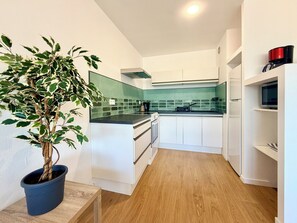 A modern kitchen with white cabinetry, a green backsplash, and a potted plant. - T2 Thermes et centre Aix-les-Bains parking (Aix-les-Bains)