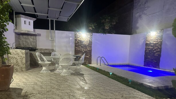 Una terrazza esterna con piscina, sedie bianche e un muro in pietra.