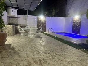 An outdoor patio with a pool, white chairs, and a stone wall.