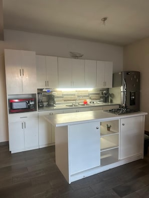 Une cuisine moderne avec des meubles blancs, un réfrigérateur en acier inoxydable, un four à micro-ondes et une cuisinière à gaz.