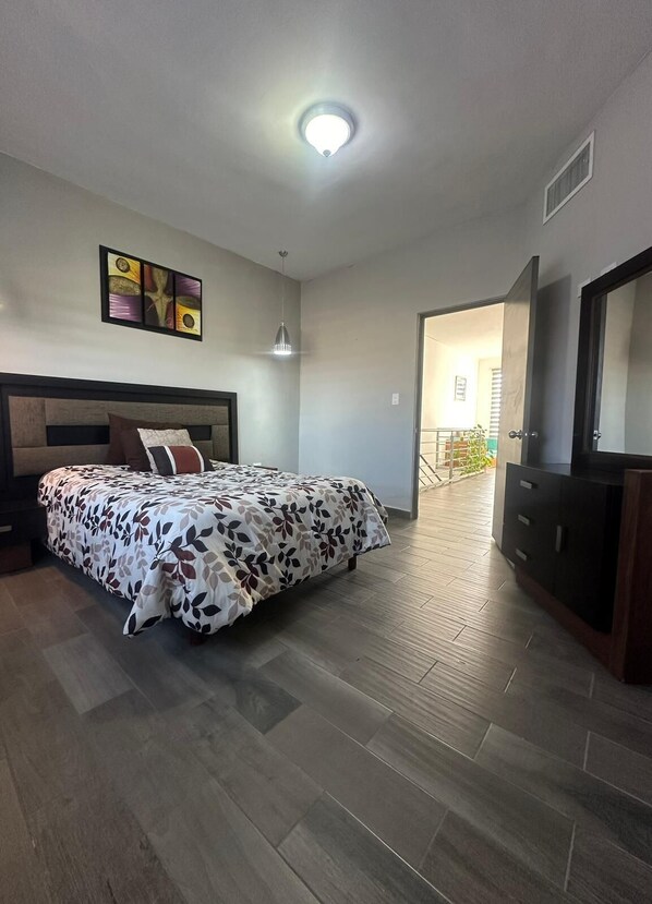 A bedroom with a bed, a dresser, a ceiling light, and a door leading to another room.