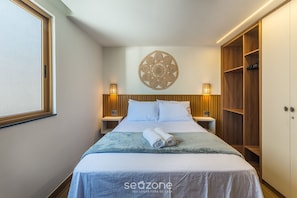 Ein ordentlich bezogenes Bett mit einem aufgerollten Handtuch, einem an der Wand befestigten dekorativen Gegenstand und einem Holzschrank.