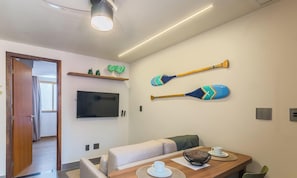 Ein modernes Wohnzimmer mit einer Couch, einem Esstisch, einem Fernseher und zwei Wanddekorationen.