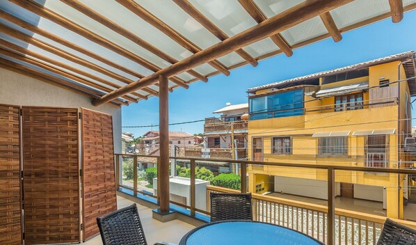 Ein Balkon mit Blick auf ein gelbes Gebäude, Korbmöbel und einem klaren Himmel.