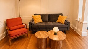 Un salon comprenant un canapé, deux petites tables en bois, un fauteuil rouge et un lampadaire.