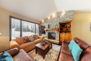 A living room with a stone fireplace, a sofa, a coffee table, and a television. - Aspens by Okanagan Premier (Beaverdell)