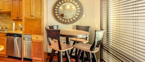 A kitchen with wooden cabinets, a stainless steel dishwasher, a round mirror, and a dining area with stools.