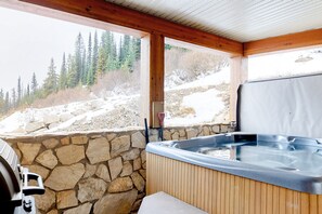 A hot tub with a stone wall and wooden beams, overlooking a snowy landscape with trees. - Aspens by Okanagan Premier (Beaverdell)