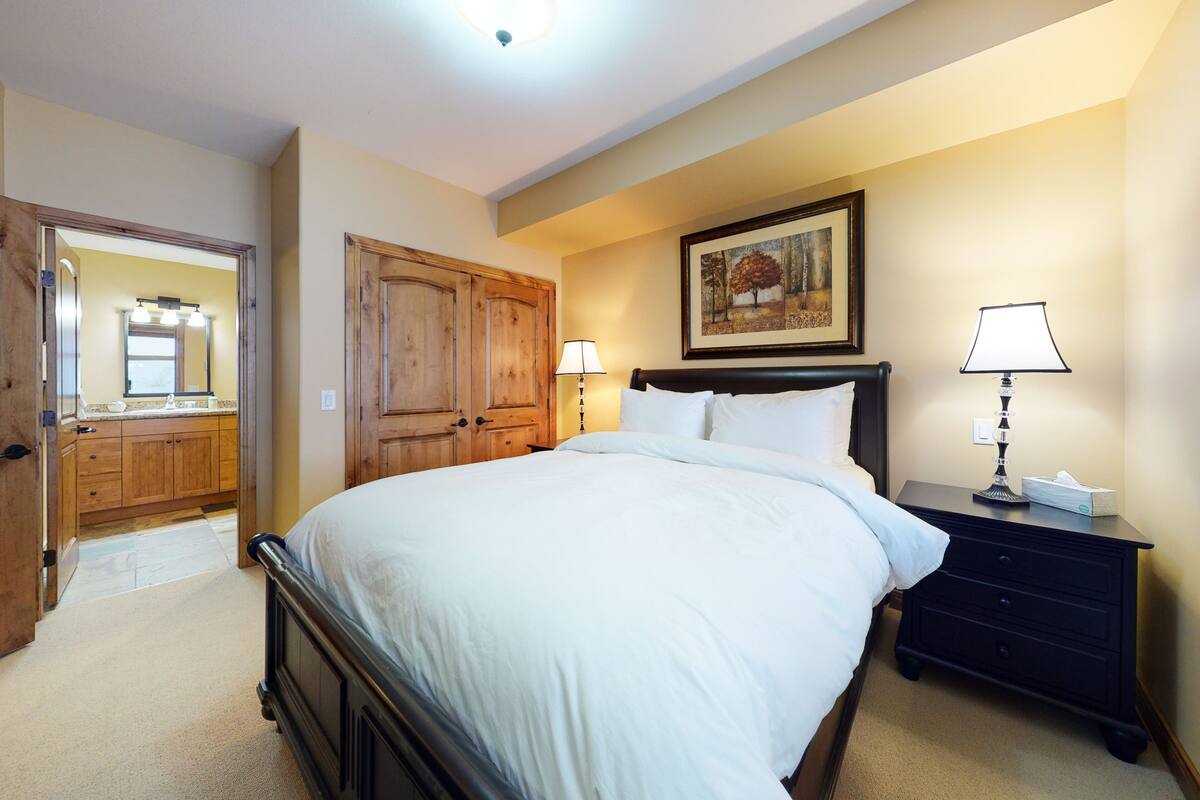 A bedroom with a large bed, wooden wardrobe, bedside table, and a mirror.