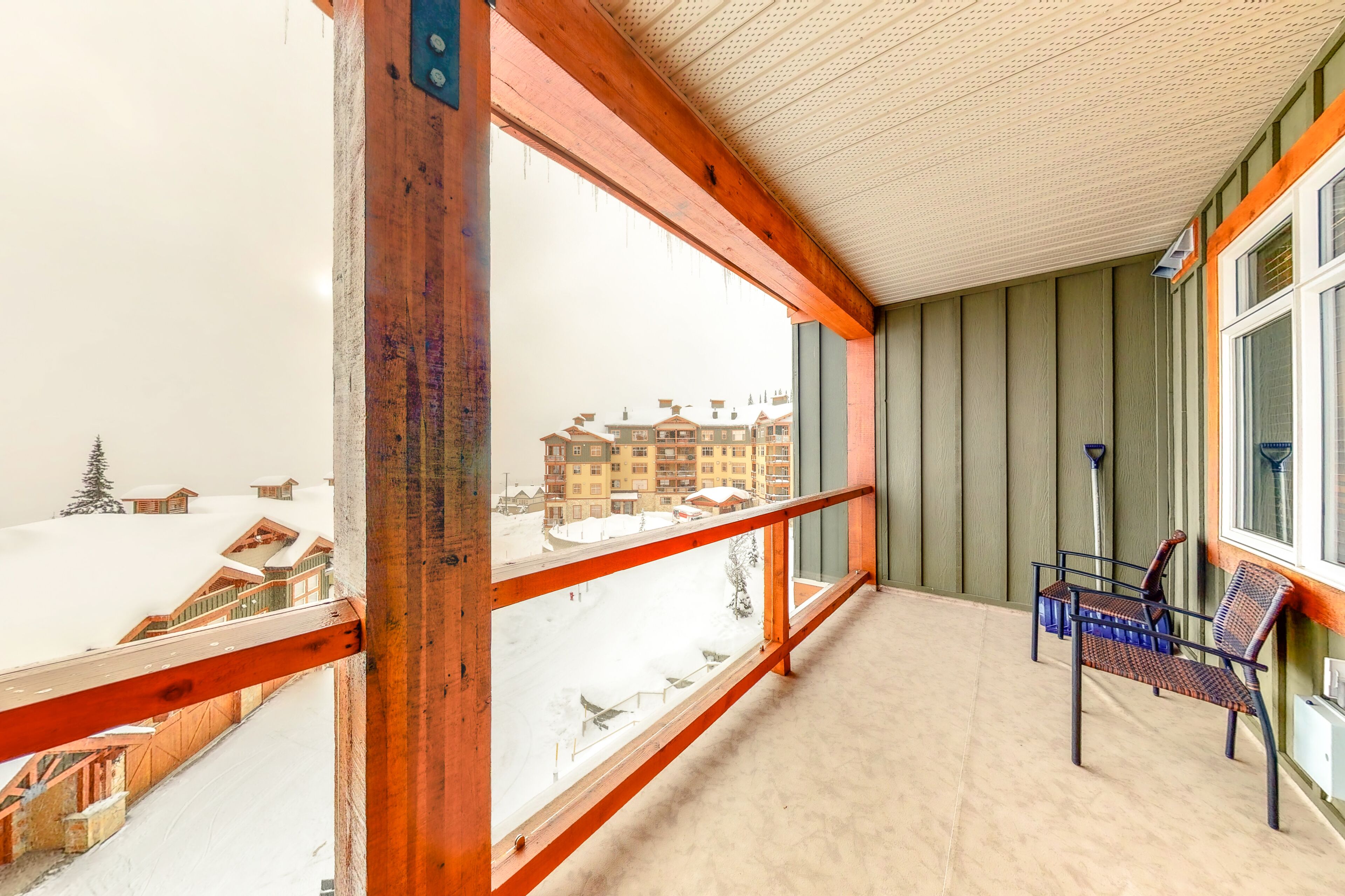 A balcony with a wooden railing, a bench, and a view of a snowy landscape with buildings.