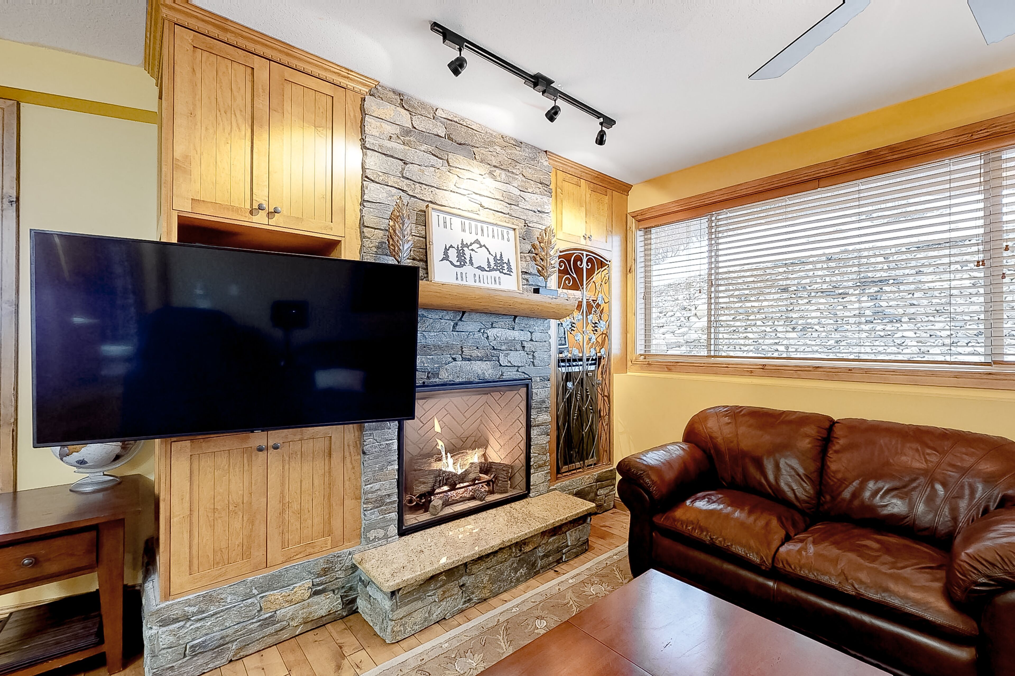 A living room with a stone fireplace, a flat-screen TV, and a leather sofa.