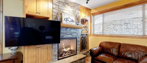 A living room with a stone fireplace, a flat-screen TV, and a leather sofa.