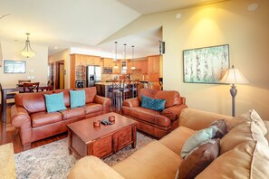 A spacious living room with leather sofas, a coffee table, and a dining area with wooden furniture. - Aspens by Okanagan Premier (Beaverdell)