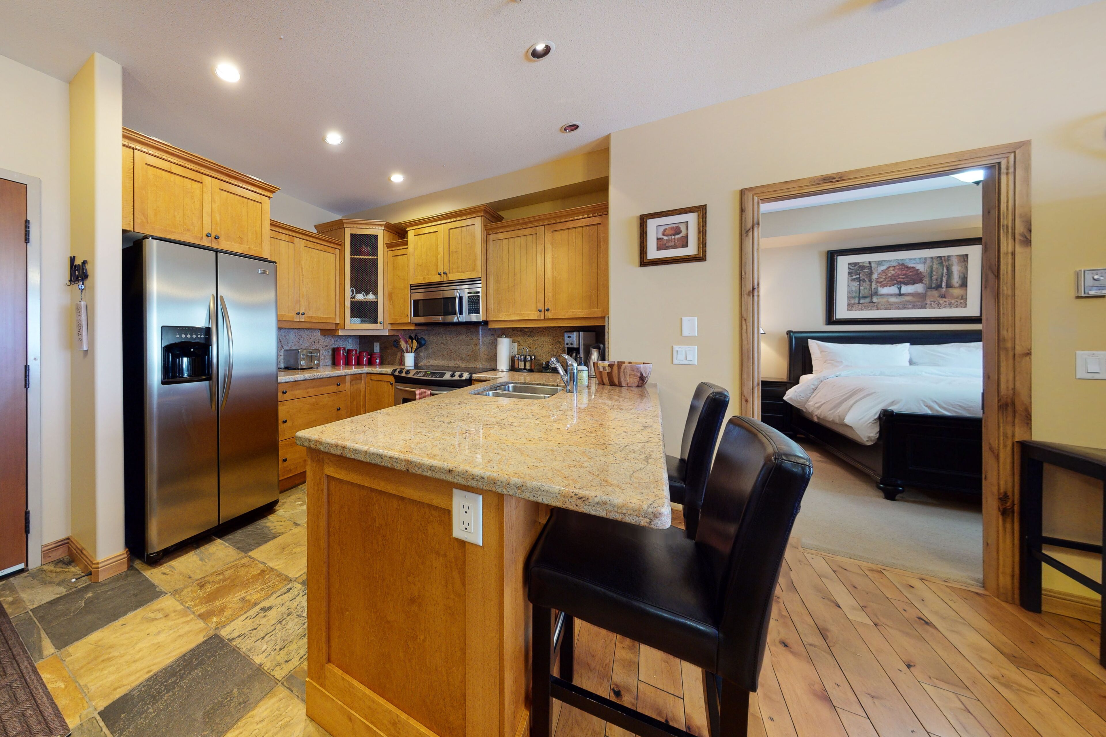A kitchen with wooden cabinets, a stainless steel refrigerator, a microwave, and a granite countertop.