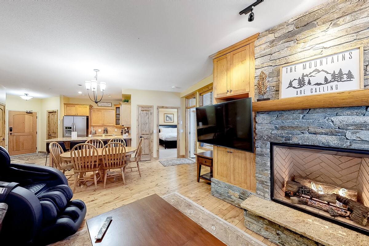 A spacious living room with a stone fireplace, wooden cabinets, and a television.
