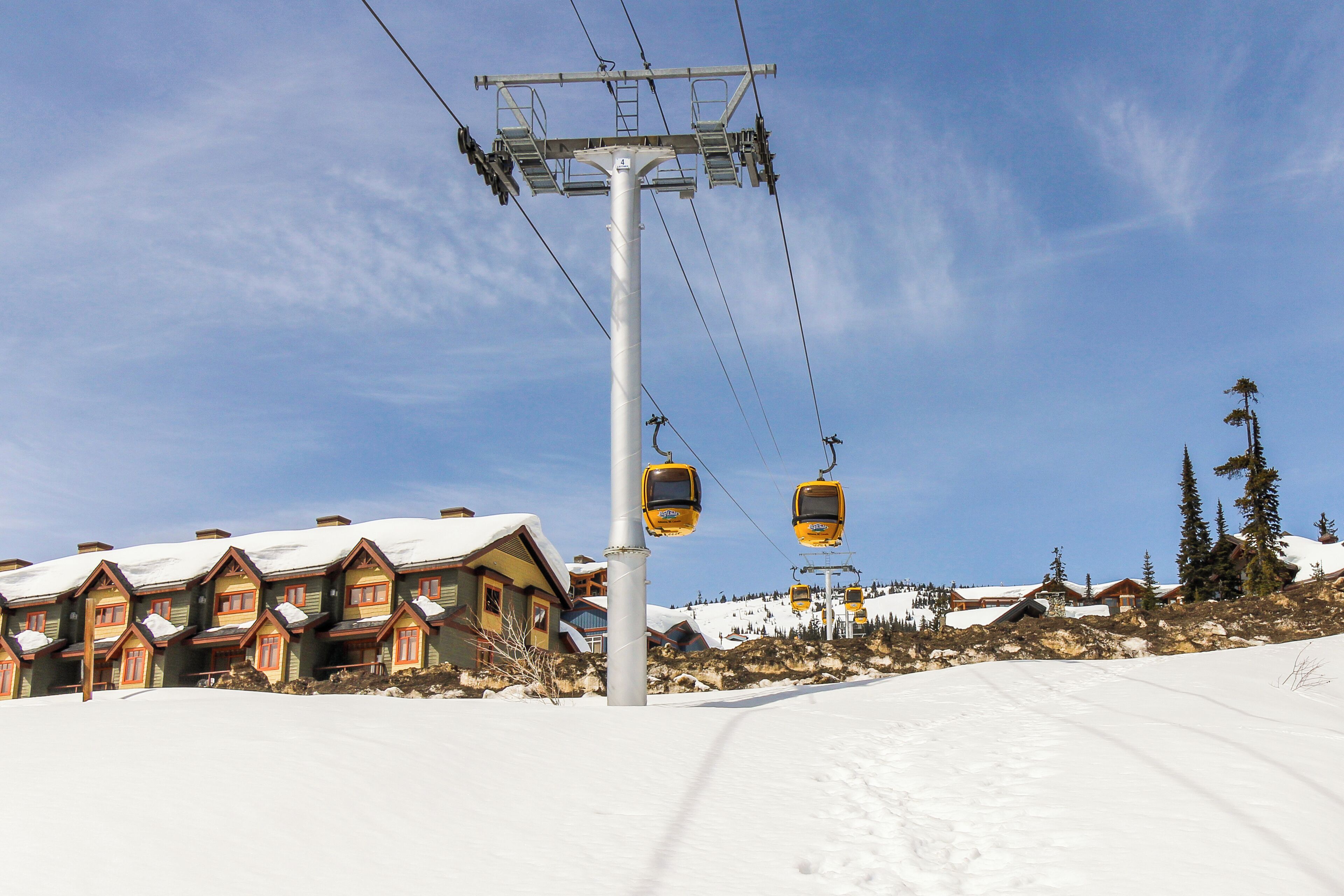 A ski lift with cabins, a snow-covered slope, and wooden buildings with snow-covered roofs.