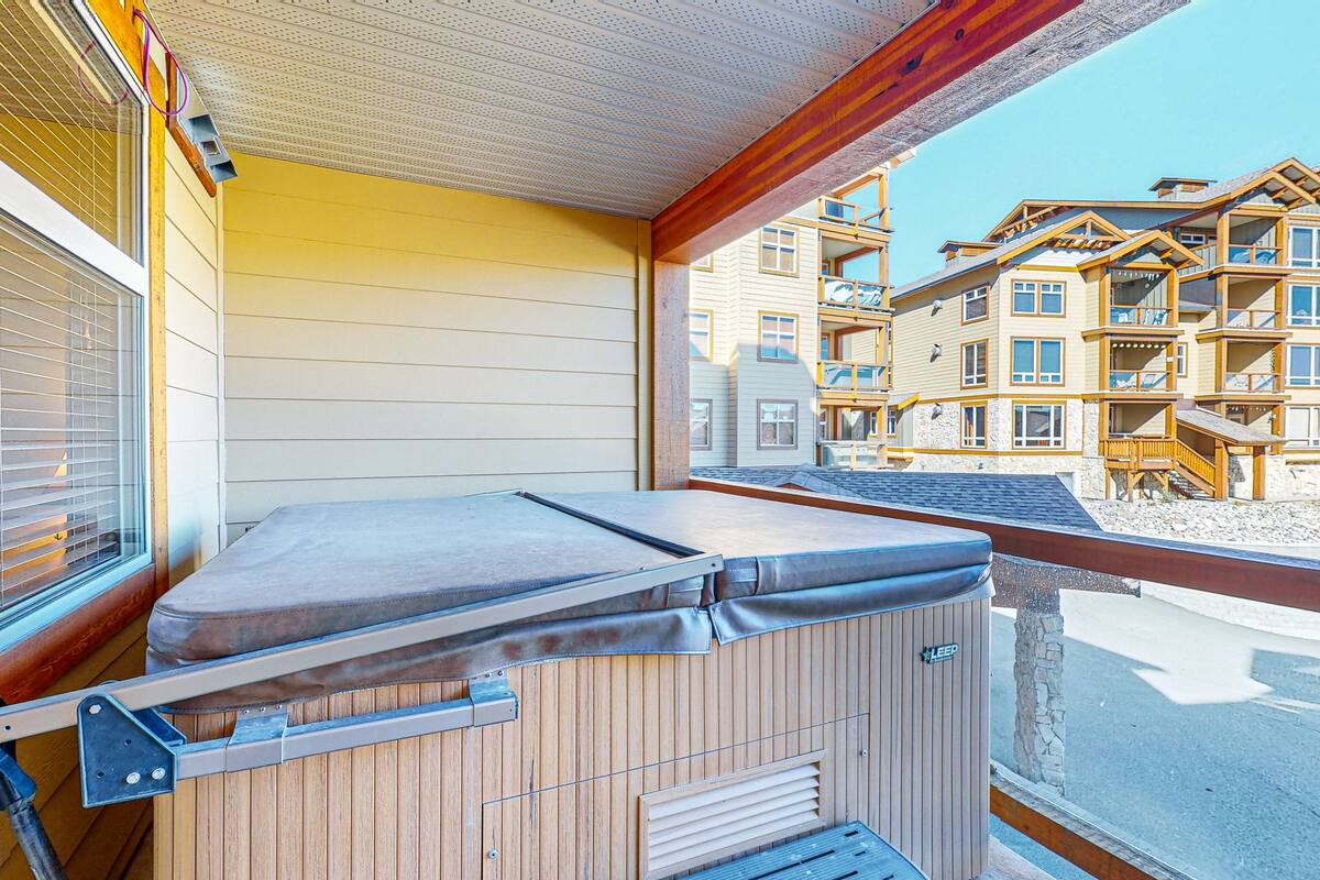 A wooden spa tub on a balcony with a view of a multi-story building.